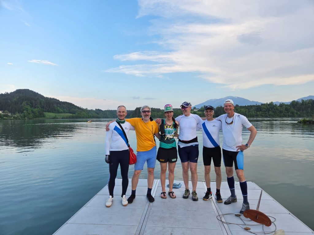 Gruppe Ruderer auf Steg vor See mit Bergkulisse. In der Mitte Magdalena Lobnig